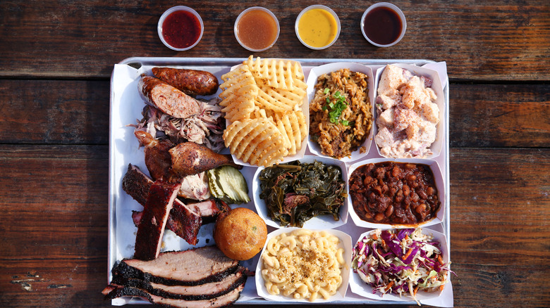 platter with barbecue ribs, brisket, sausage, and an array of sides including greens, fries, cole slaw, baked beans, and potato salad.