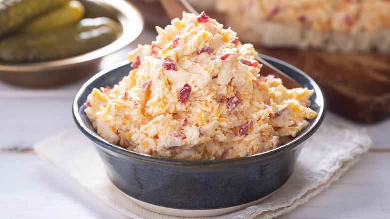 a black ramekin of pimento cheese on a white table.