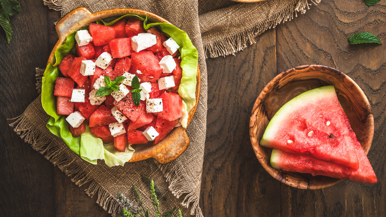 a watermelon salad with feta, black pepper, and mint next to two slices of watermelon.