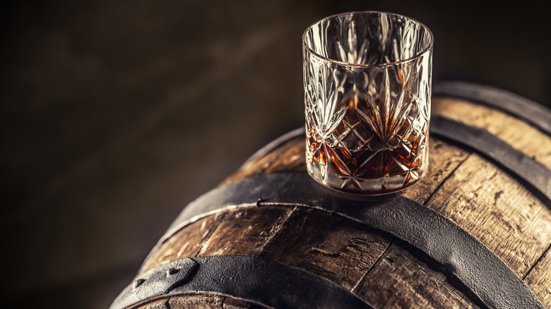 A glass of whiskey sitting on a barrel