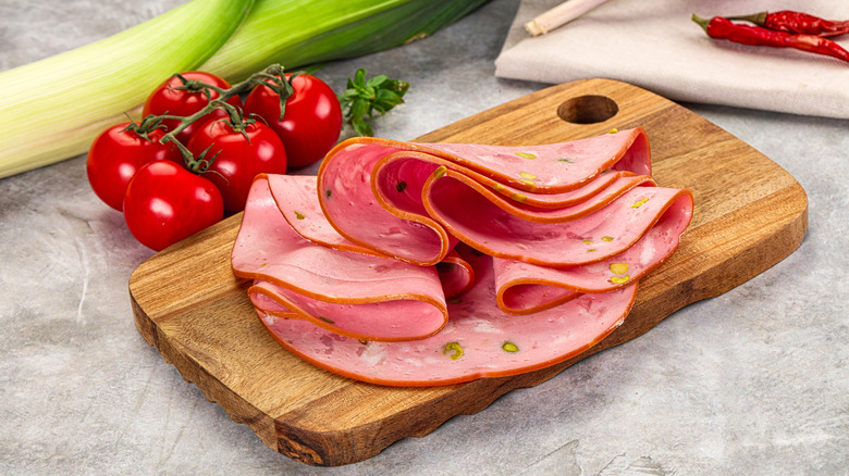 Mortadella pork sausages slices heap over board.