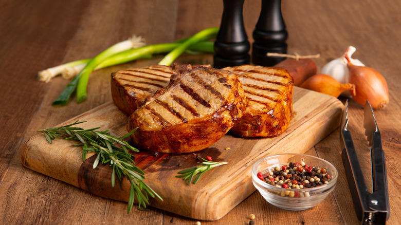 Juicy pork chops on a wooden board with scattered herbs and seasonings