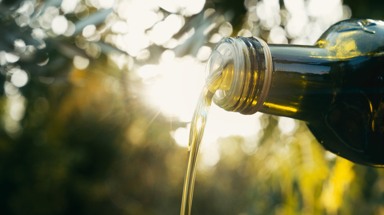 Olive oil being poured from a glass bottle in an outdoor setting