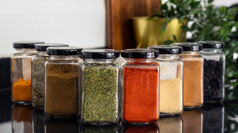 Various spice jars on a black countertop with greenery in the background