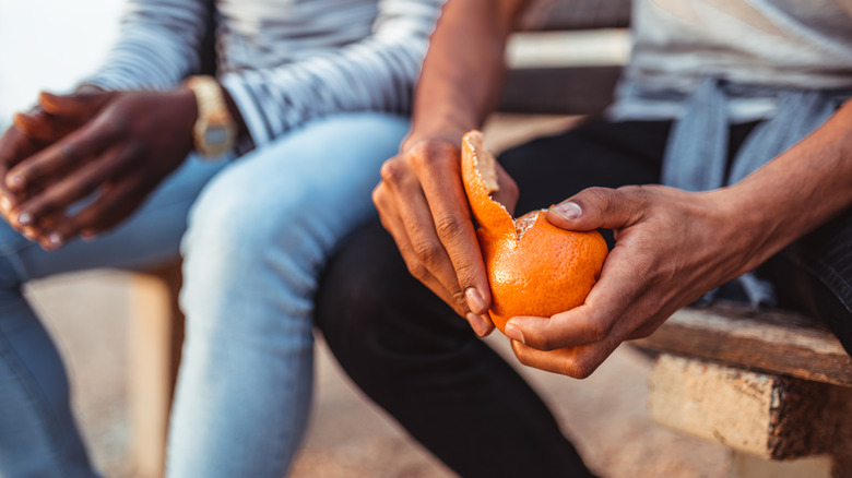 Man sitting in public, peeling an orange