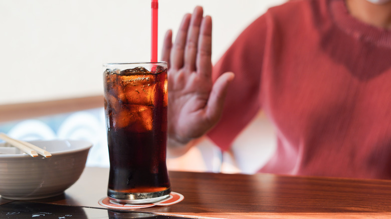 Someone holding up a hand to reject a soft drink