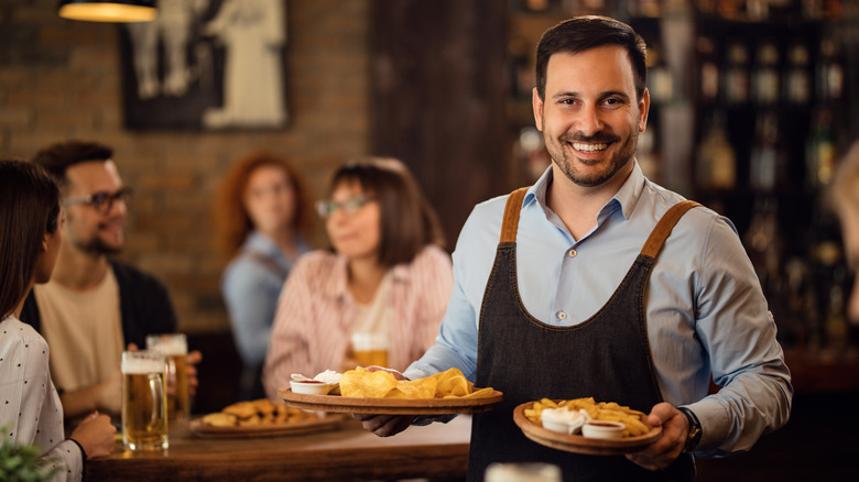 A grinning man waiting tables with plates